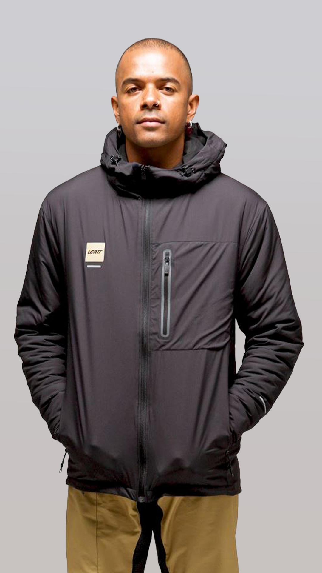 Man wearing a dark gray jacket with a hood on a gray background